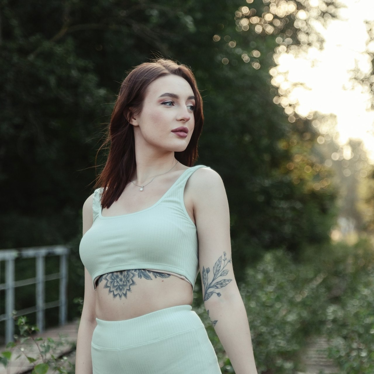 Woman in a mint-green outfit standing outdoors on a tree-lined path at sunset