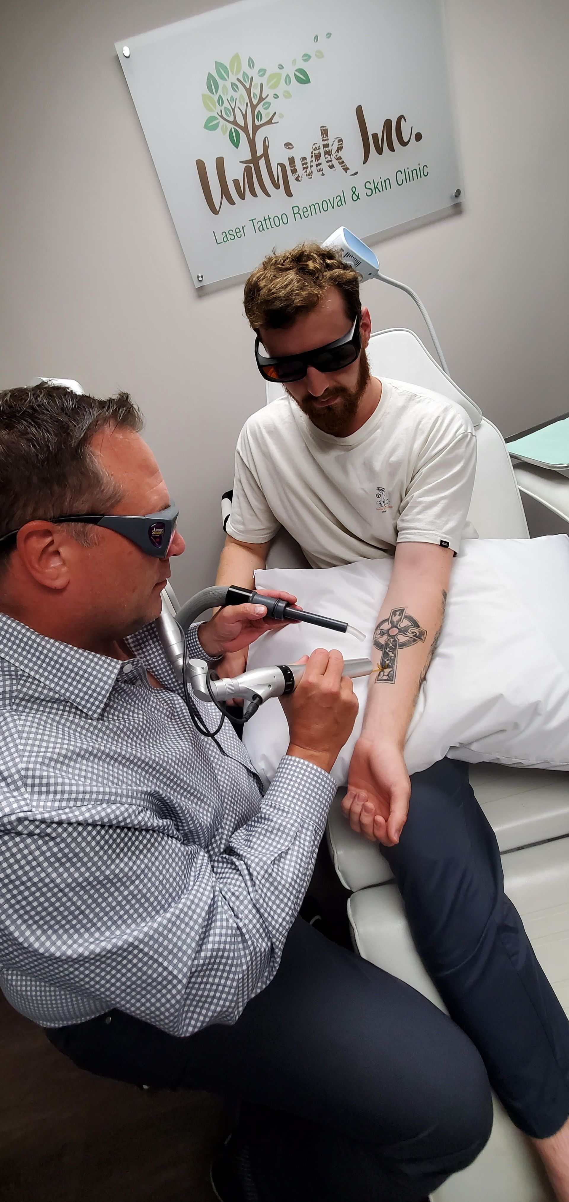 Two people at a clinic, one examining the other's arm while they sit on a chair.