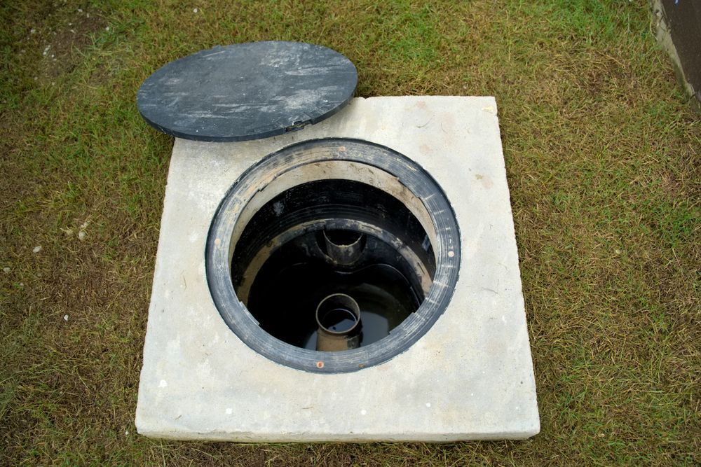 Open Manhole in a Concrete Slab With the Round Cover Set Aside on Grass — Evans Earthmoving Contractors In Malanda, QLD 