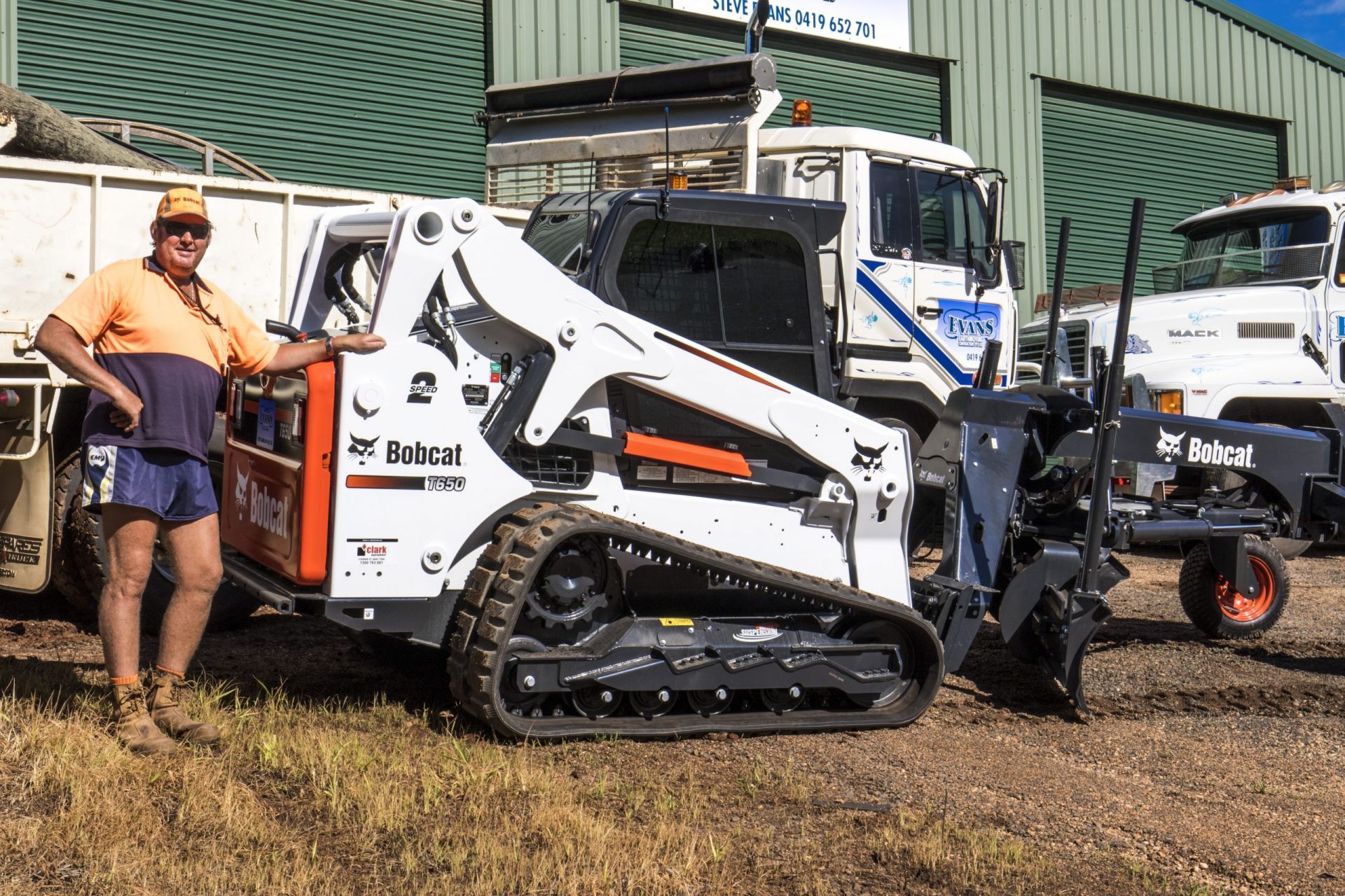 Man Standing Beside a White Bobcat Skid-steer Loader — Evans Earthmoving Contractors In Malanda, QLD