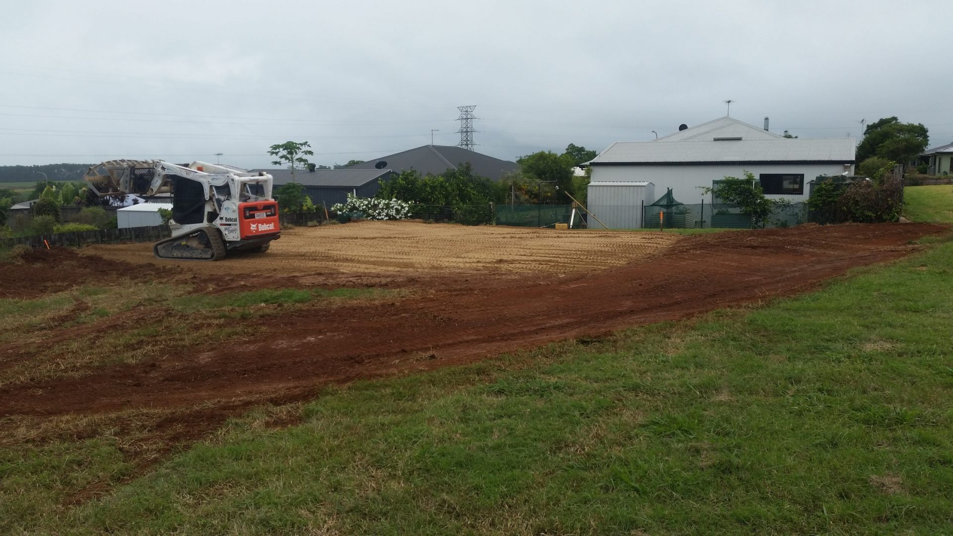 A Small Bulldozer Grading a Cleared Plot of Land, with Houses and Cloudy Sky in The Background — Evans Earthmoving Contractors In Malanda, QLD 
