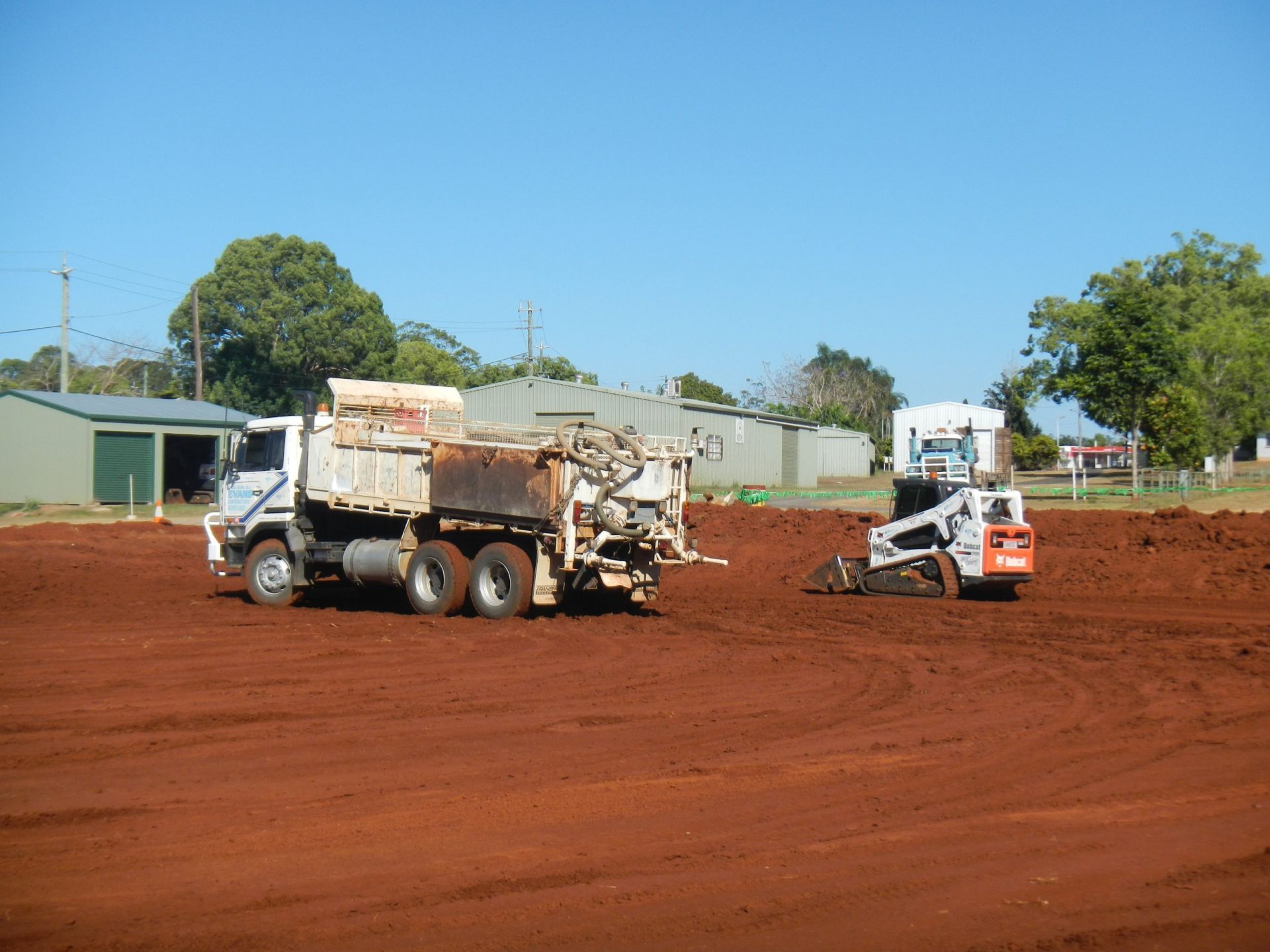 A Truck and A Skid Steer Are on A Red Dirt Field, Likely for Construction — Evans Earthmoving Contractors In Malanda, QLD 