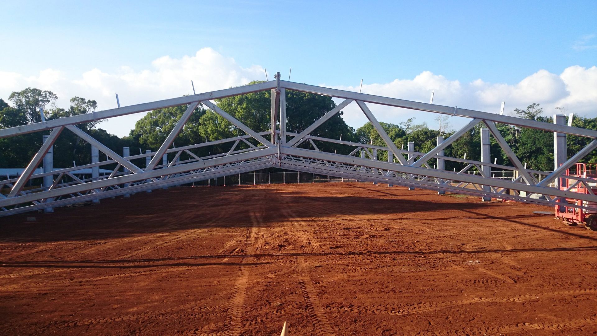 Steel Framework of A White Arch Structure on Brown Dirt Under a Blue Sky — Evans Earthmoving Contractors In Malanda, QLD 