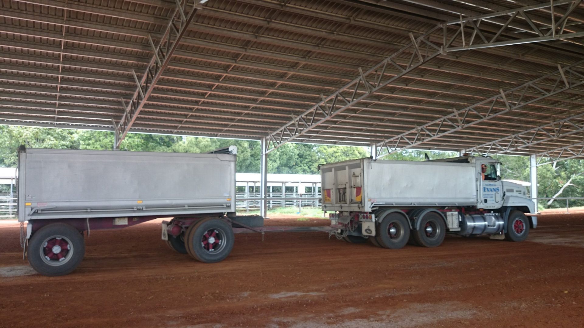 Truck and Trailer Parked Under a Metal Roof Structure on A Red Dirt Surface — Evans Earthmoving Contractors In Malanda, QLD 