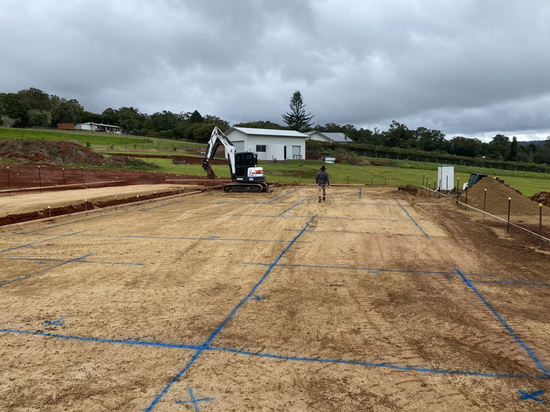 Construction Site: Excavator and Person on Dirt Lot Marked with Blue Lines — Evans Earthmoving Contractors In Malanda, QLD 