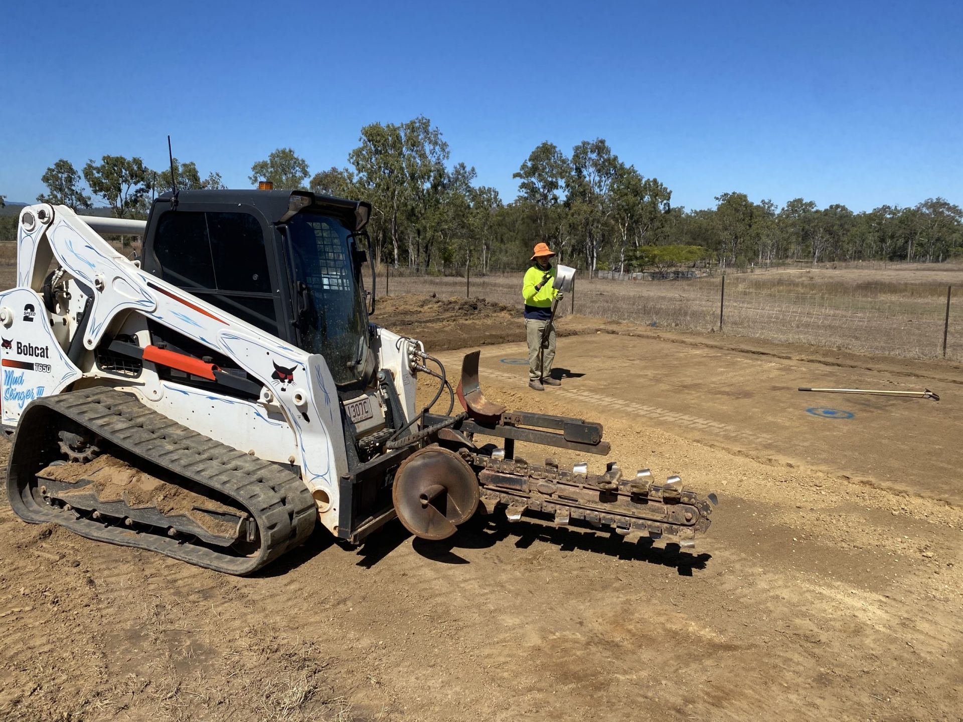 Bobcat Skid Steer with A Chain Attachment; Worker with Orange Hardhat in Field — Evans Earthmoving Contractors In Malanda, QLD
