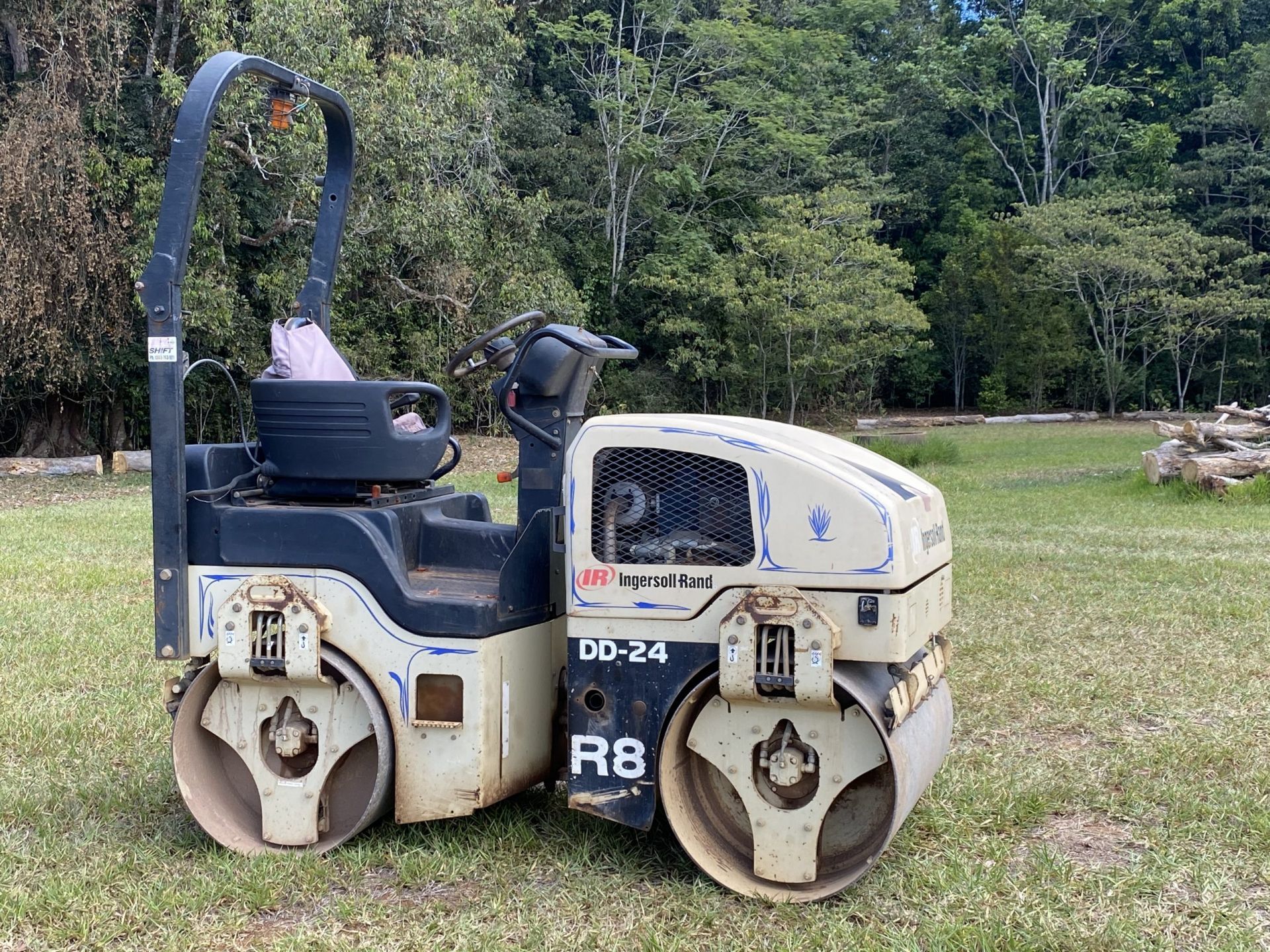 A Small, Beige Road Roller on Green Grass with A Forest Background — Evans Earthmoving Contractors In Malanda, QLD 