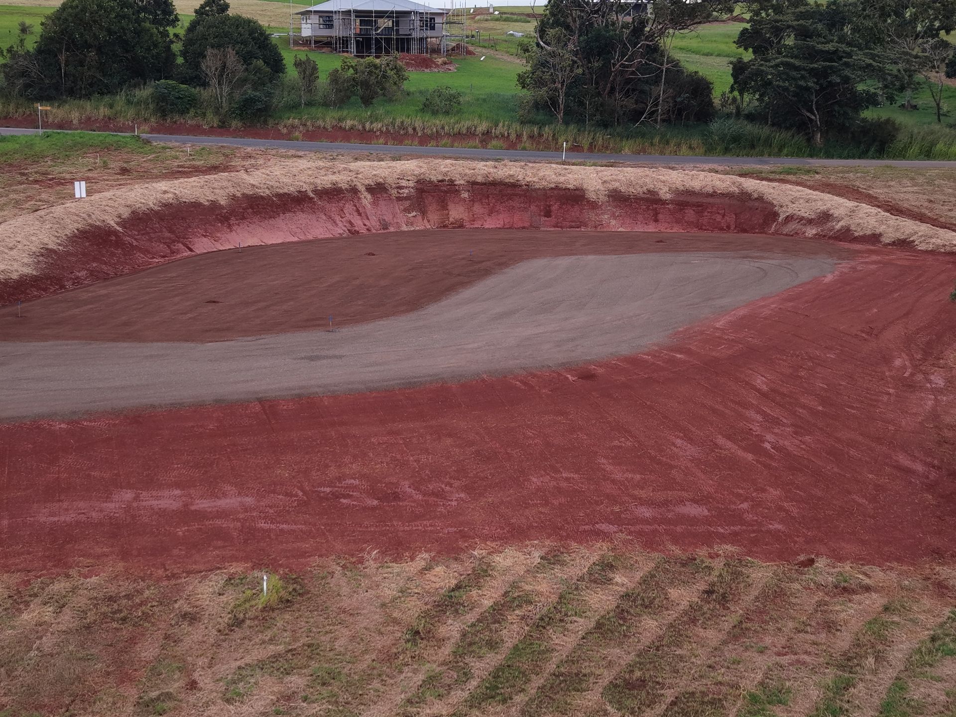 Freshly graded red dirt field with a grey center, bordered by grass and trees in the background — Evans Earthmoving Contractors In Malanda, QLD 