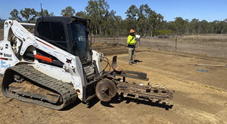 White Bobcat Trencher Digging on A Dirt Road, Person in A Vest Stands Nearby — Evans Earthmoving Contractors In Malanda, QLD 