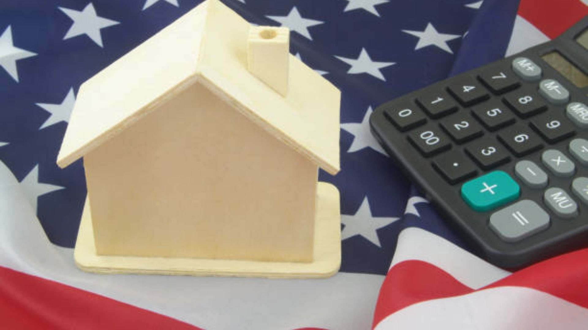 A small house is sitting next to a calculator on an american flag.