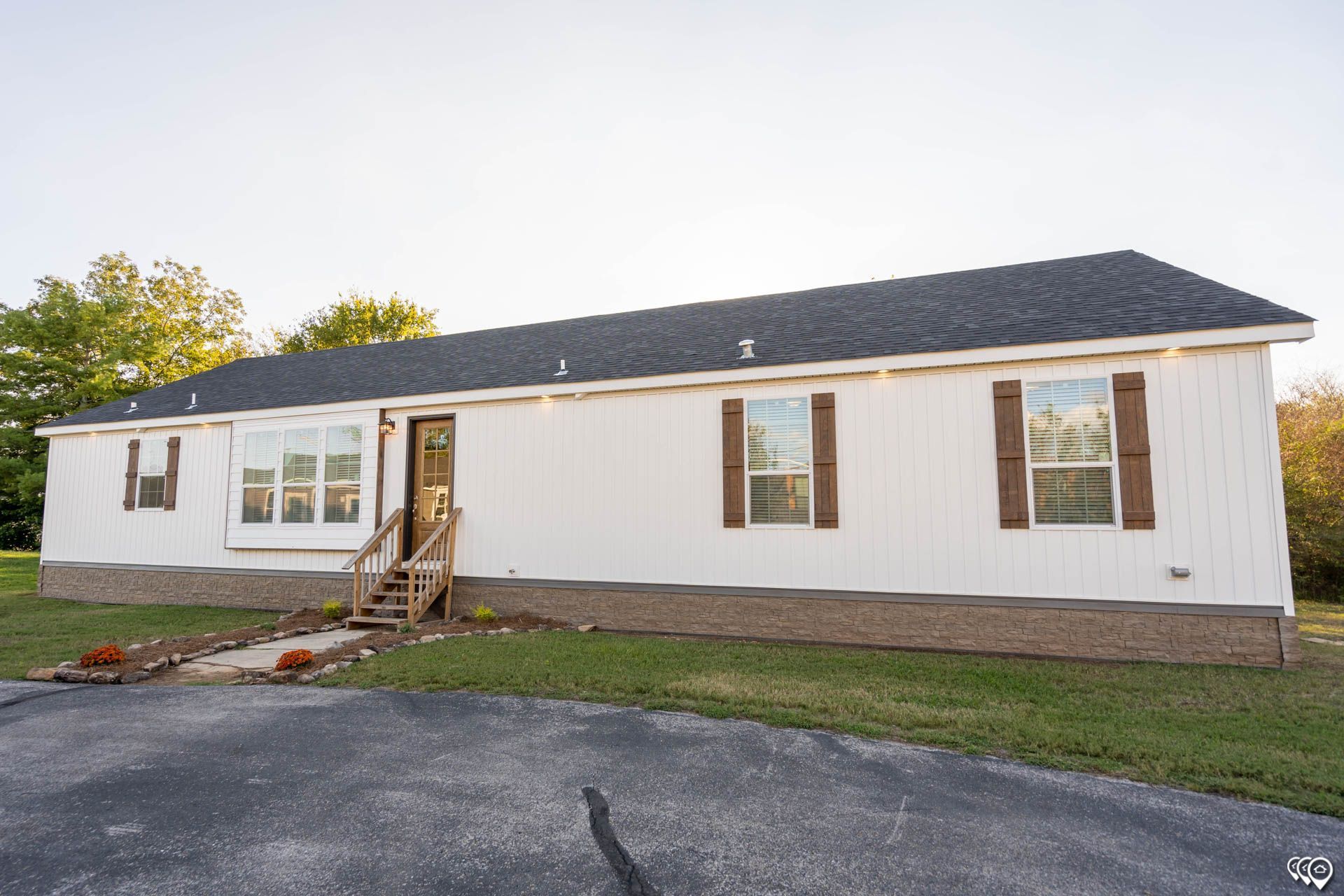White single-story house with dark roof and brown shutters on a grassy lot, paved driveway.