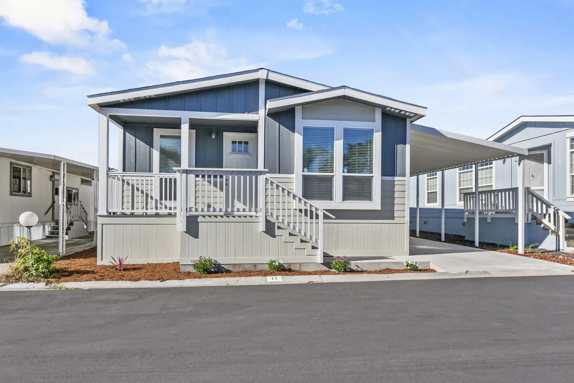 “Modern manufactured home with covered front porch, carport, and landscaped exterior in a residentia