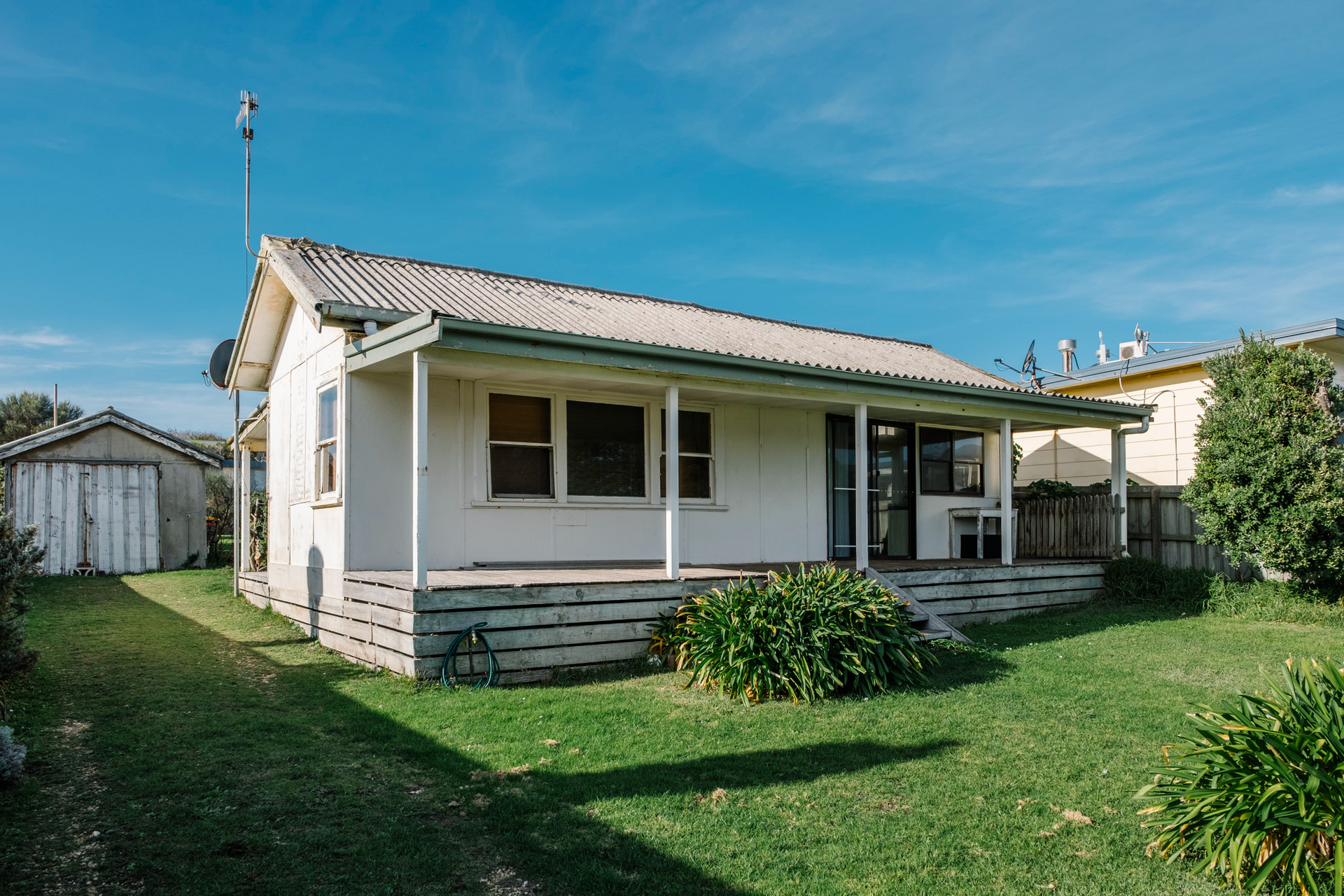 Older single-story home with a covered front porch, weathered exterior, and large grassy yard