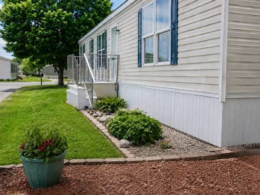 Well-maintained manufactured home with vinyl siding, exterior windows, landscaped yard, and front