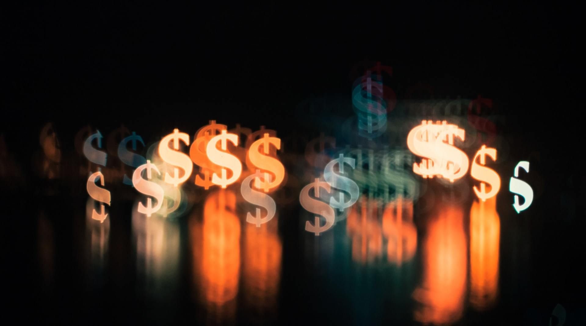 A row of dollar signs are reflected in a dark room.