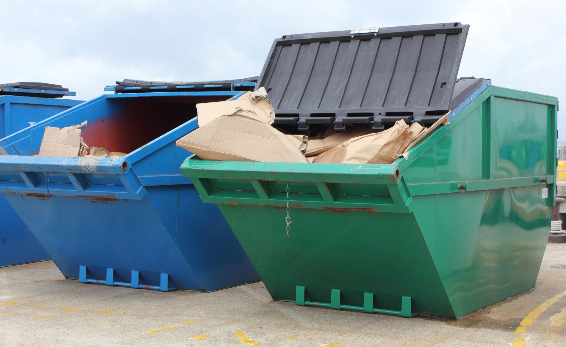Three industrial blue and green waste skips placed side-by-side. Three industrial blue and green waste skips placed side-by-side.