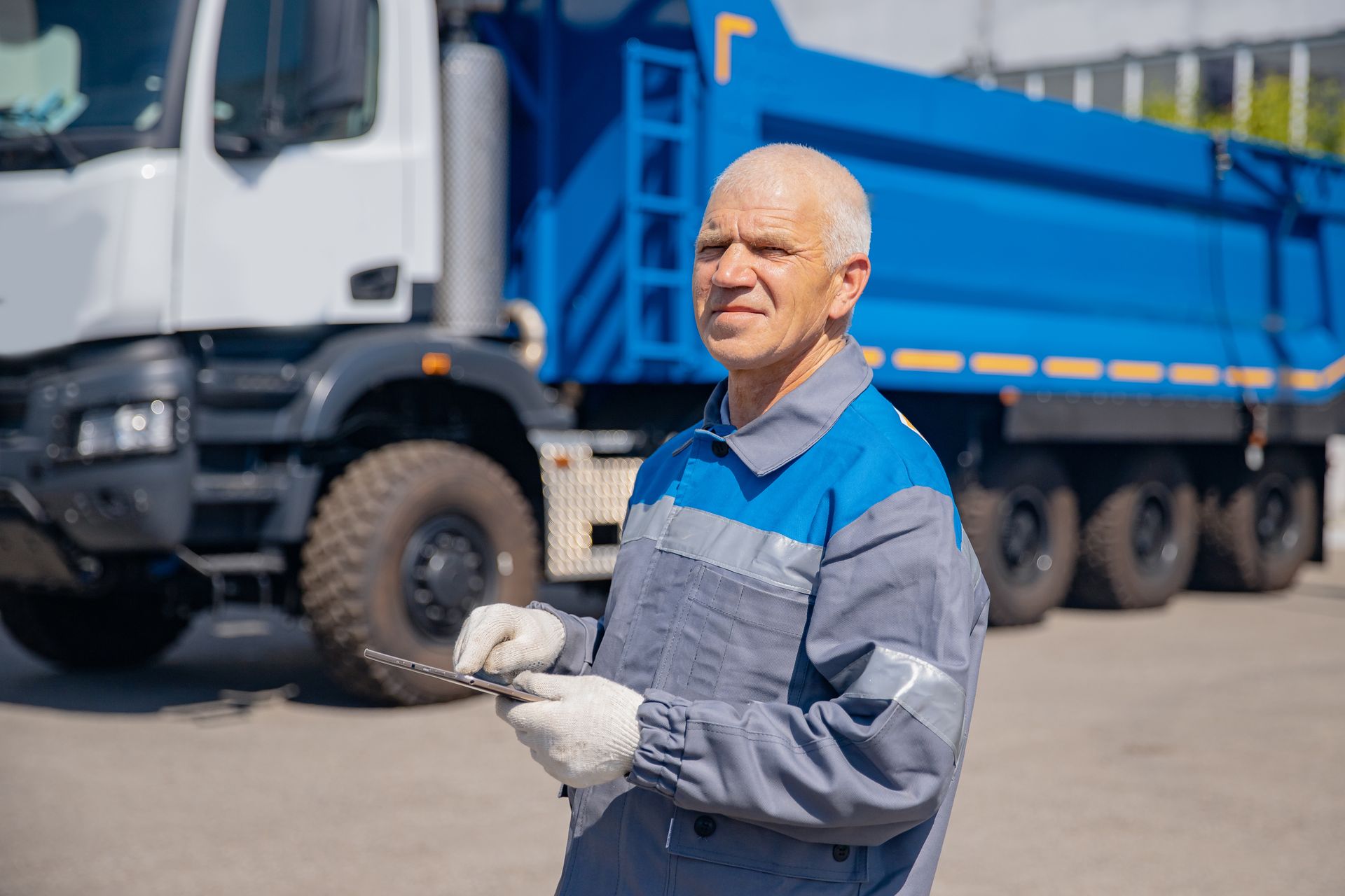 A rubbish removal driver in uniform with a tablet and a rubbish removal truck behind him.