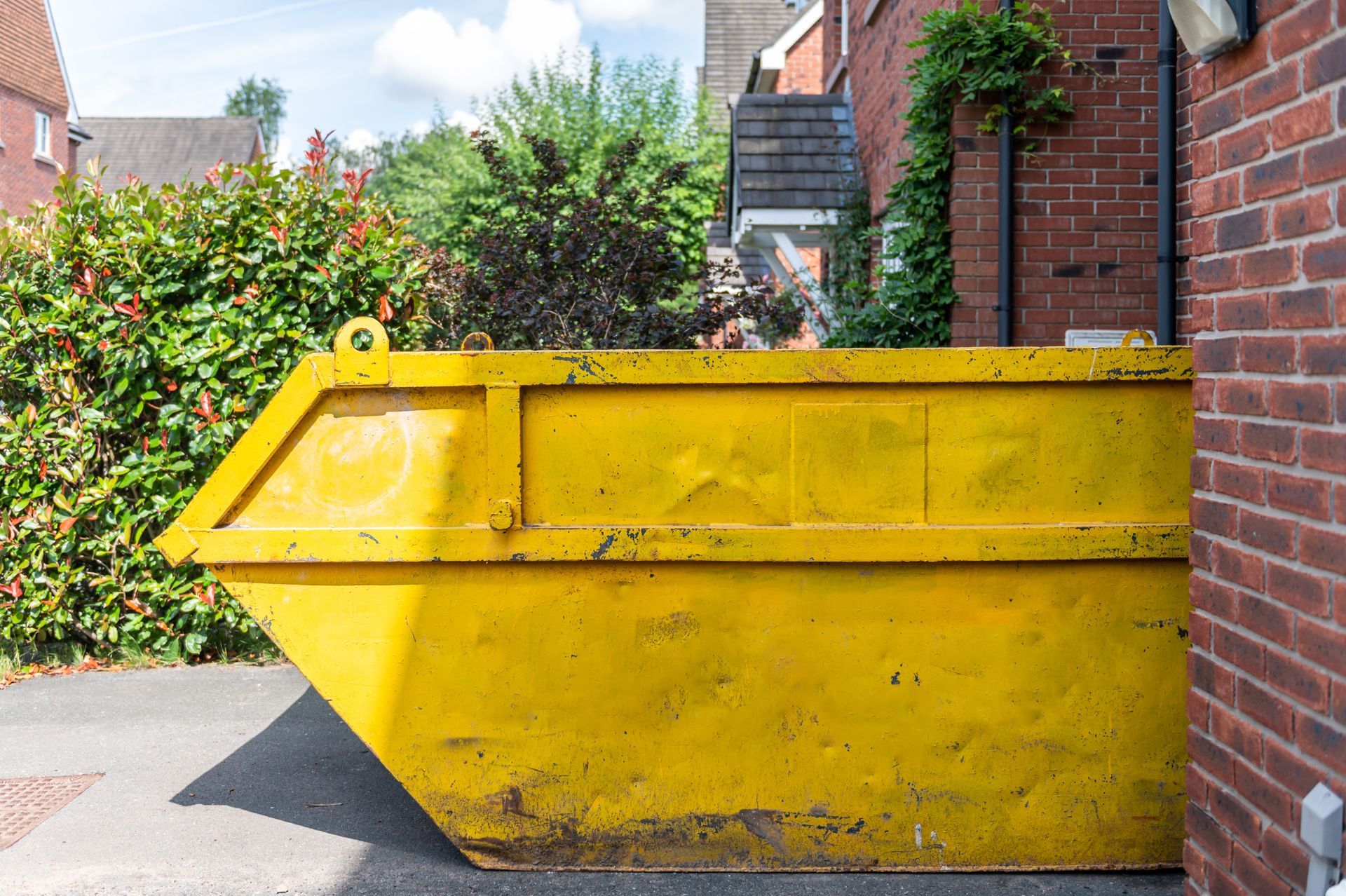 A side view of a yellow skip bin parked outside a brick-walled home. A side view of a yellow skip bin parked outside a brick-walled home.