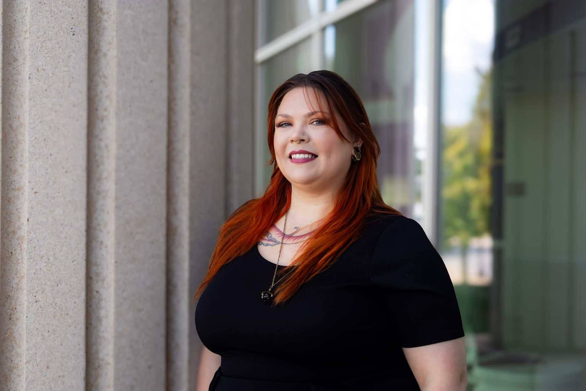 Woman with red hair and black top smiles next to a light-colored pillar.