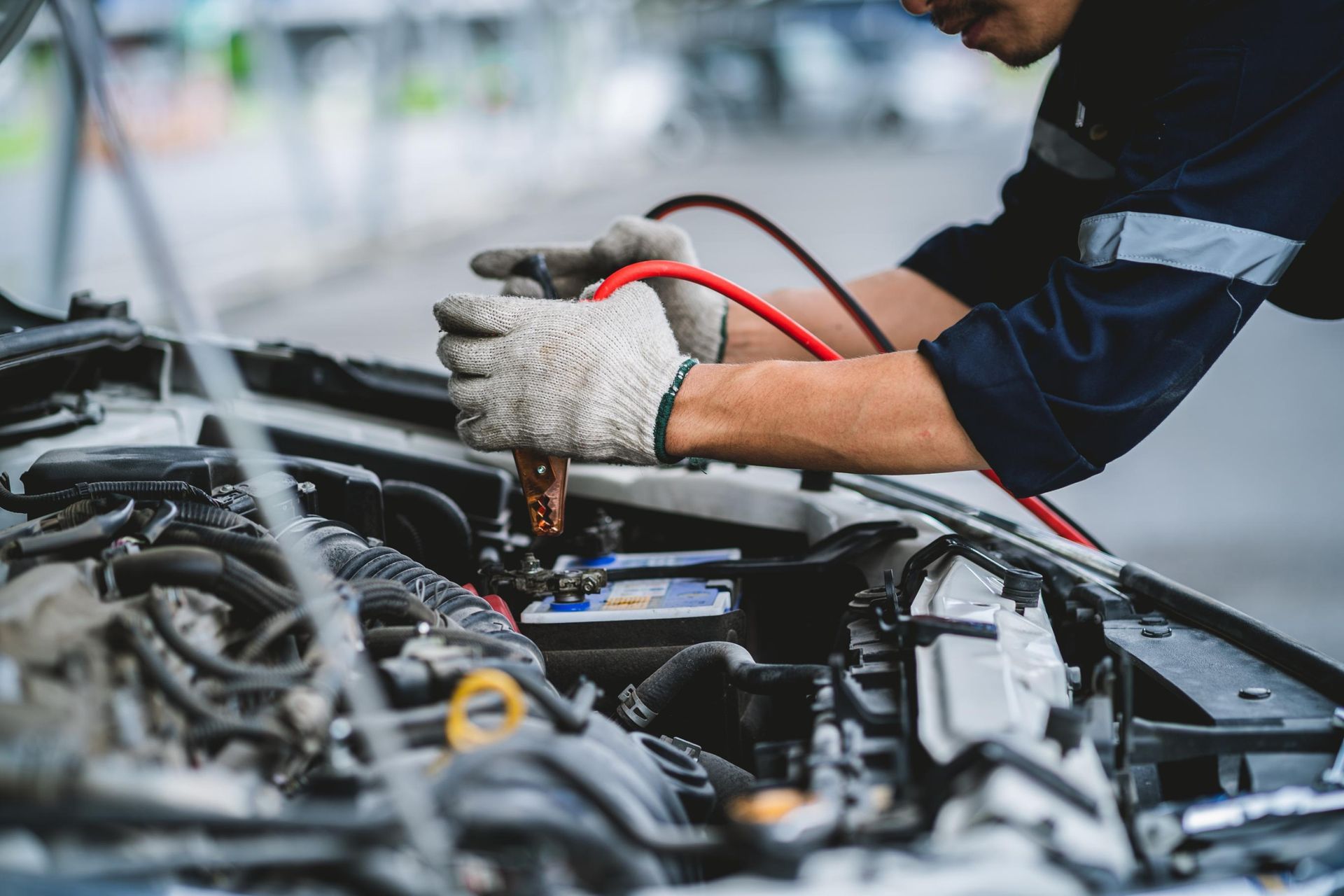 Mechanic wearing gloves repairing a car engine with jumper cables in a garage