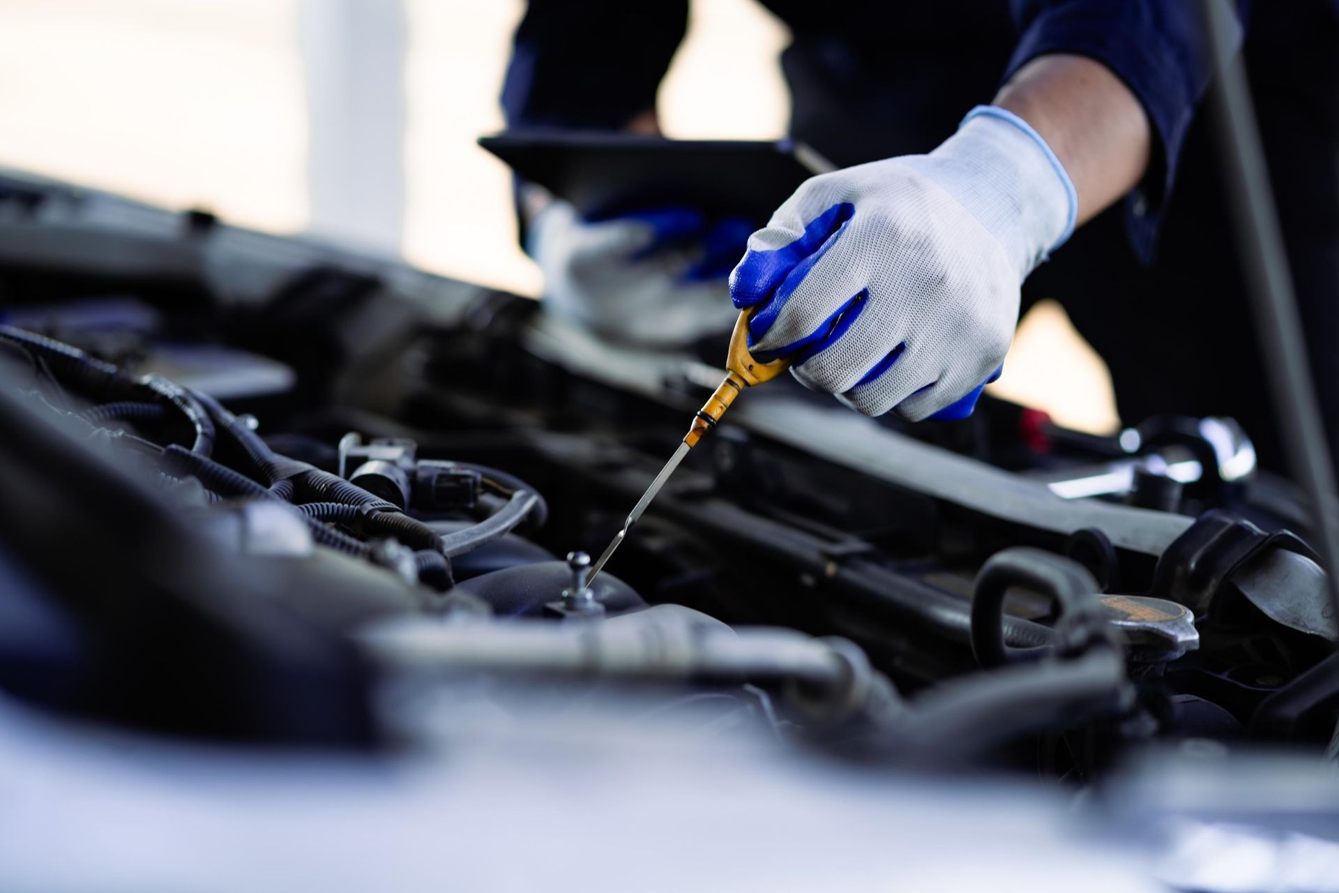 Gloved hands using a dipstick to check engine oil in a car engine bay