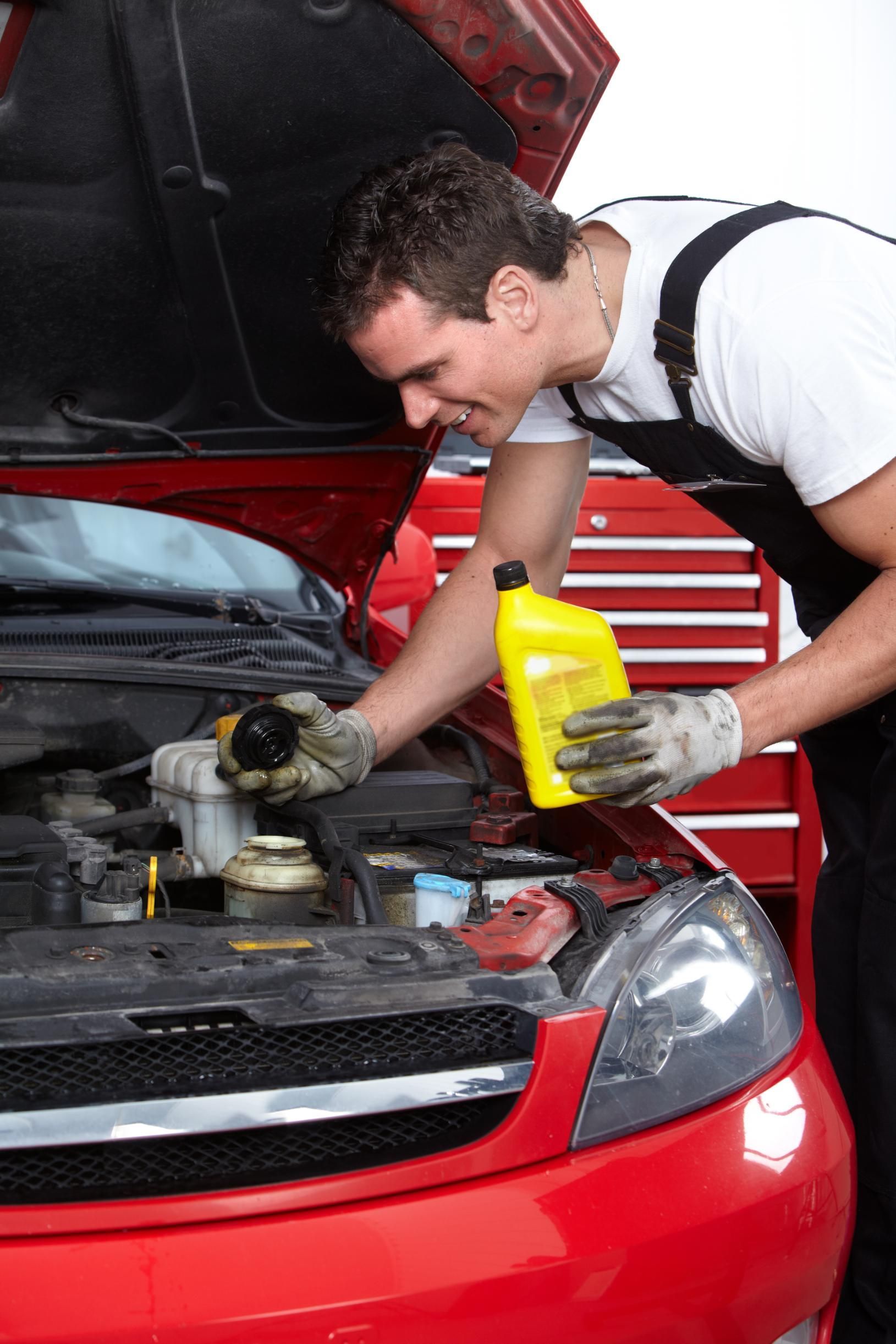 Mechanic in gloves checking engine under open hood of red car with yellow oil bottle