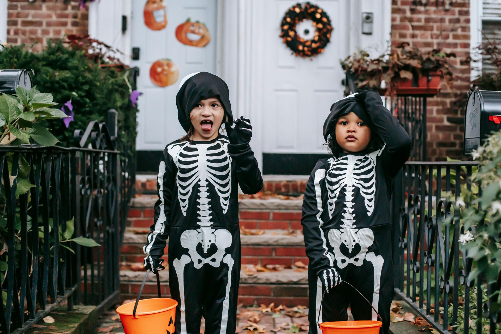 Two children in skeleton costumes are trick or treating in front of a house.