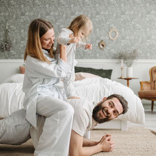 A man is laying on the floor while a woman holds a child on his shoulders.