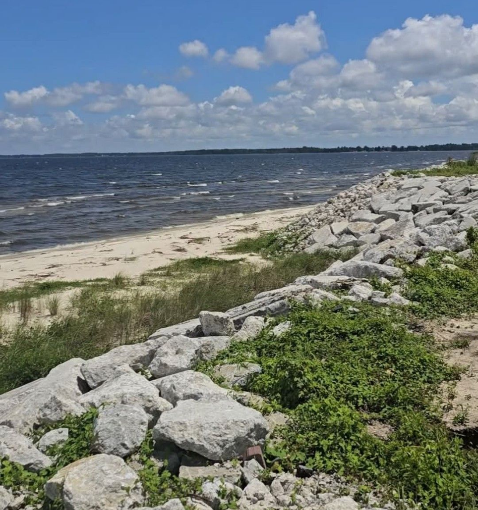 Rocky shoreline with a sandy beach, blue water, and cloudy sky.