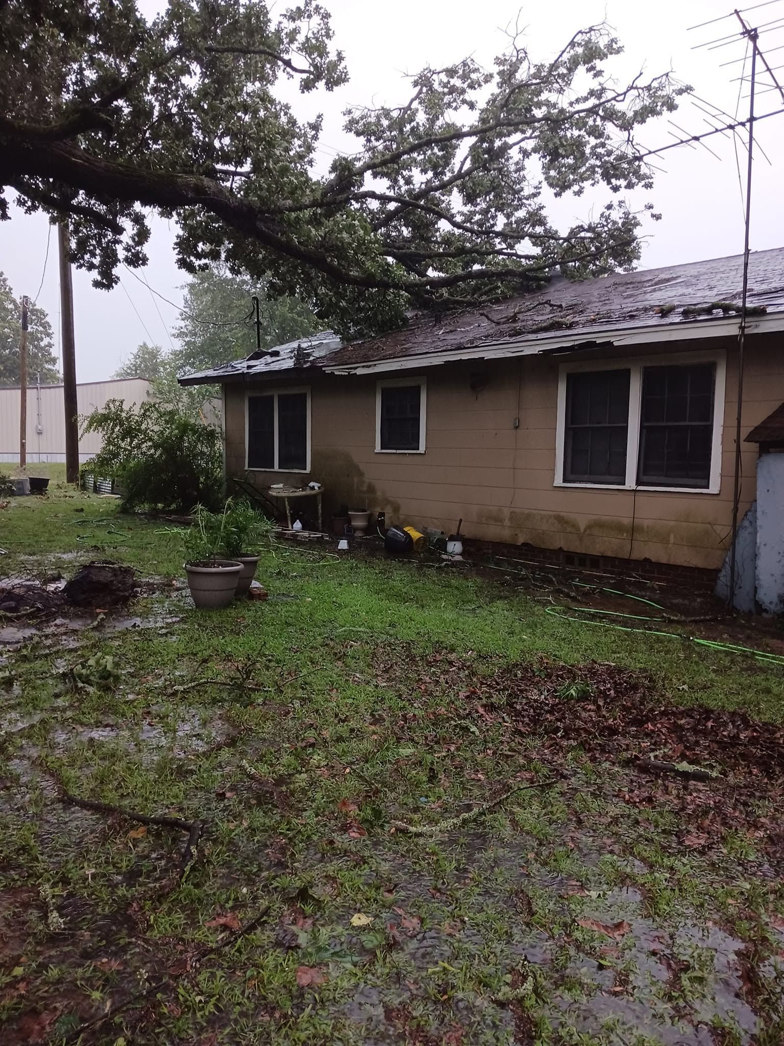 Rain-soaked yard beside a tan house with dark windows and a satellite dish