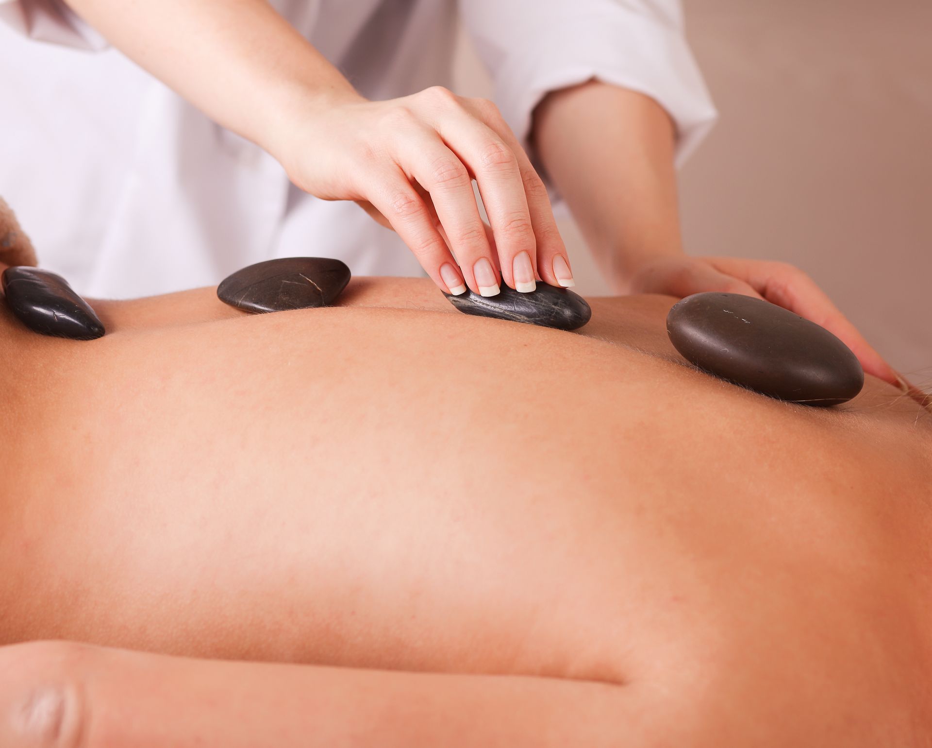 A therapist places smooth, dark heated stones on a client's back during a spa treatment.