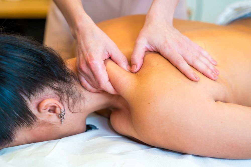 Massage therapist pressing a client’s shoulders during a spa massage on a white table