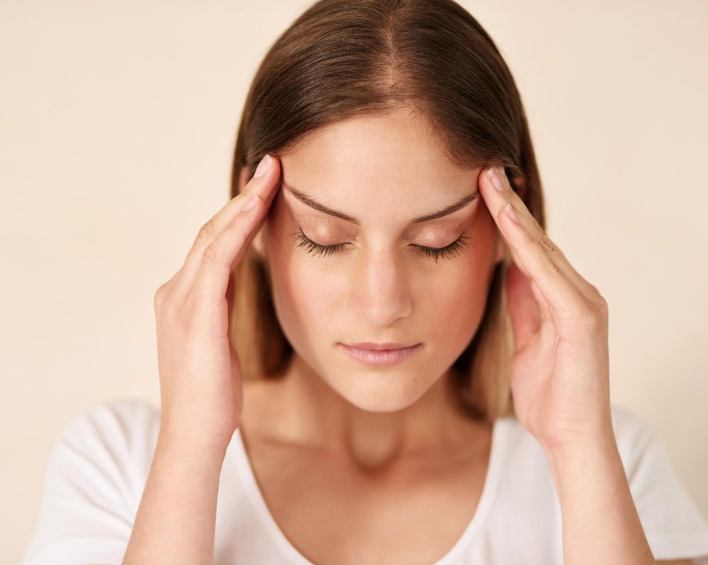 Woman pressing temples with eyes closed, appearing stressed or in pain against a light background