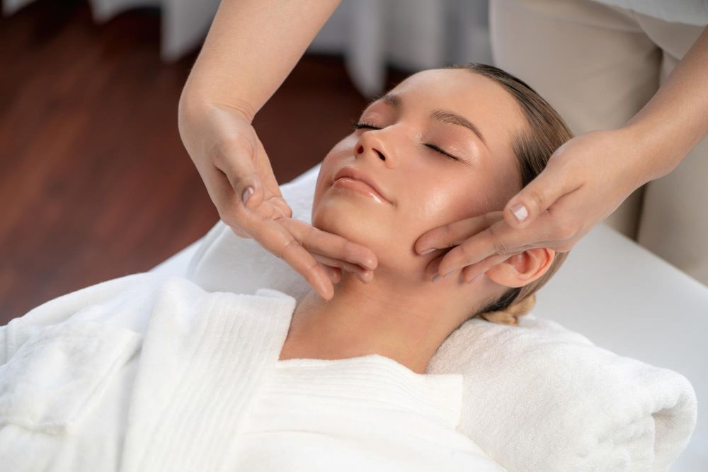 Facial massage on a woman lying on a treatment bed with a white towel