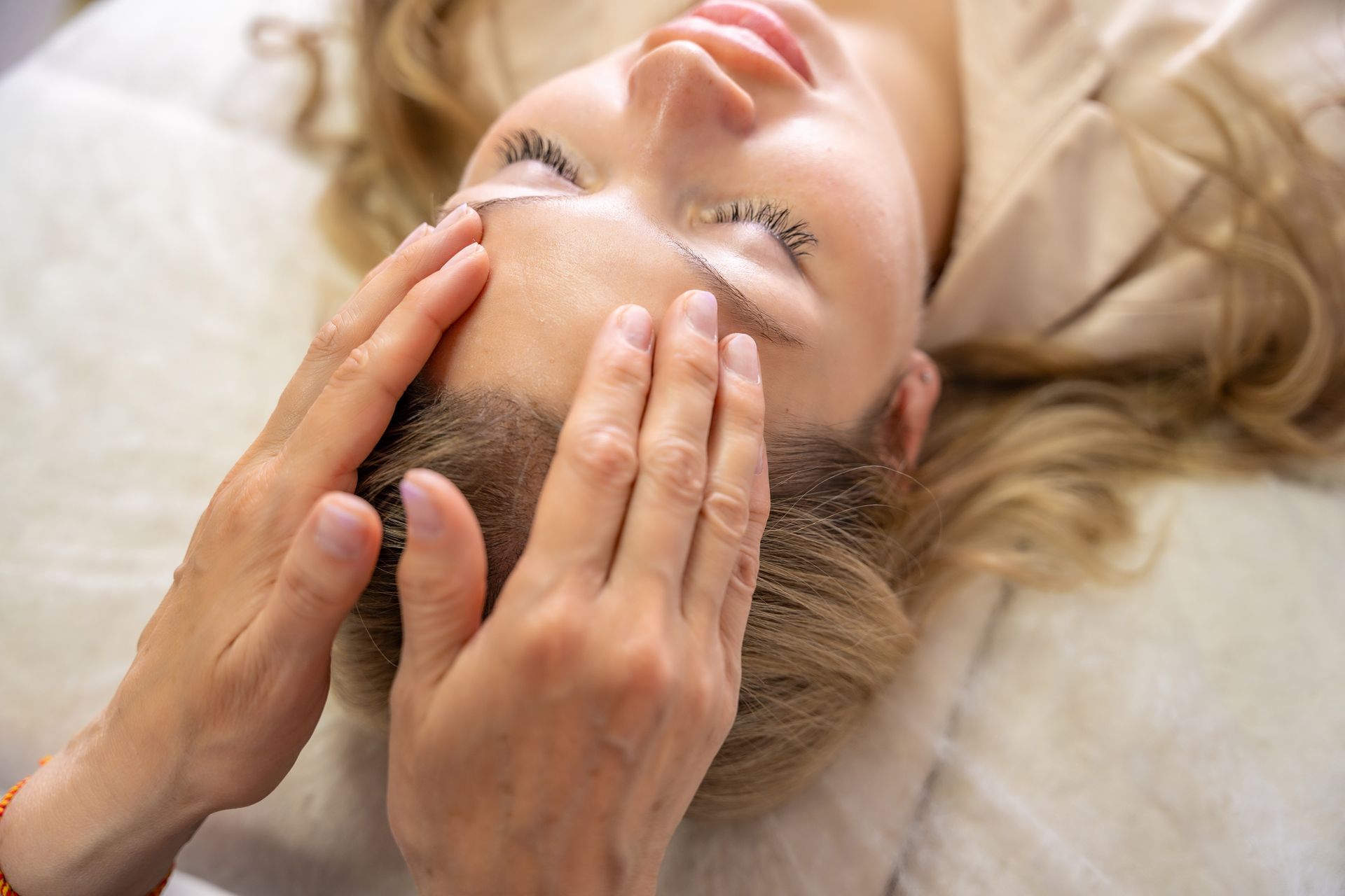 A person receives a relaxing facial massage, with hands gently touching the forehead while lying on a soft surface.