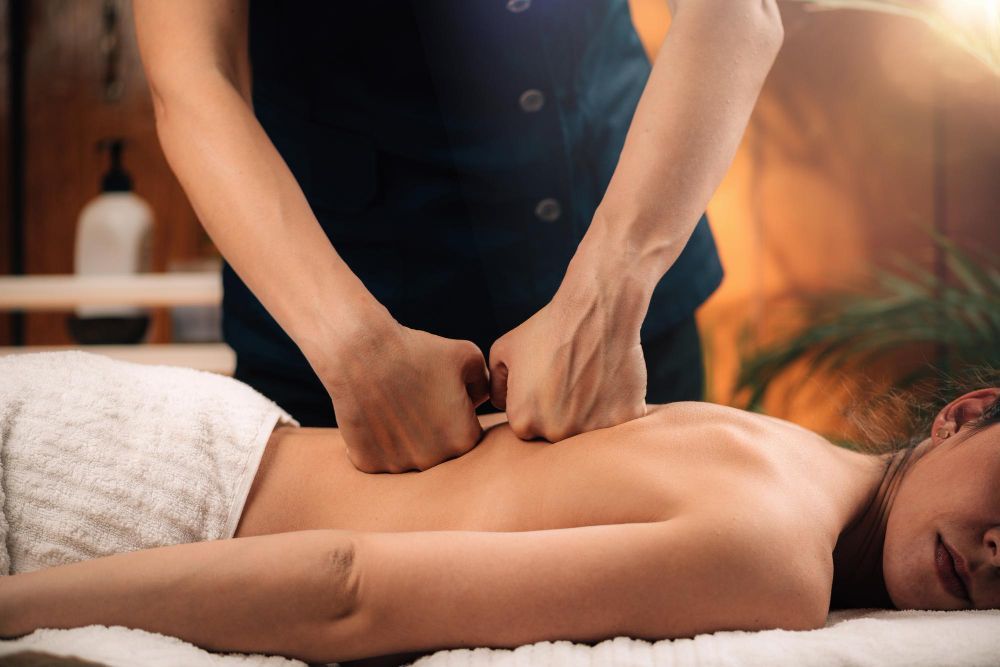 Massage therapist pressing a client's back during a spa treatment in a warm, softly lit room