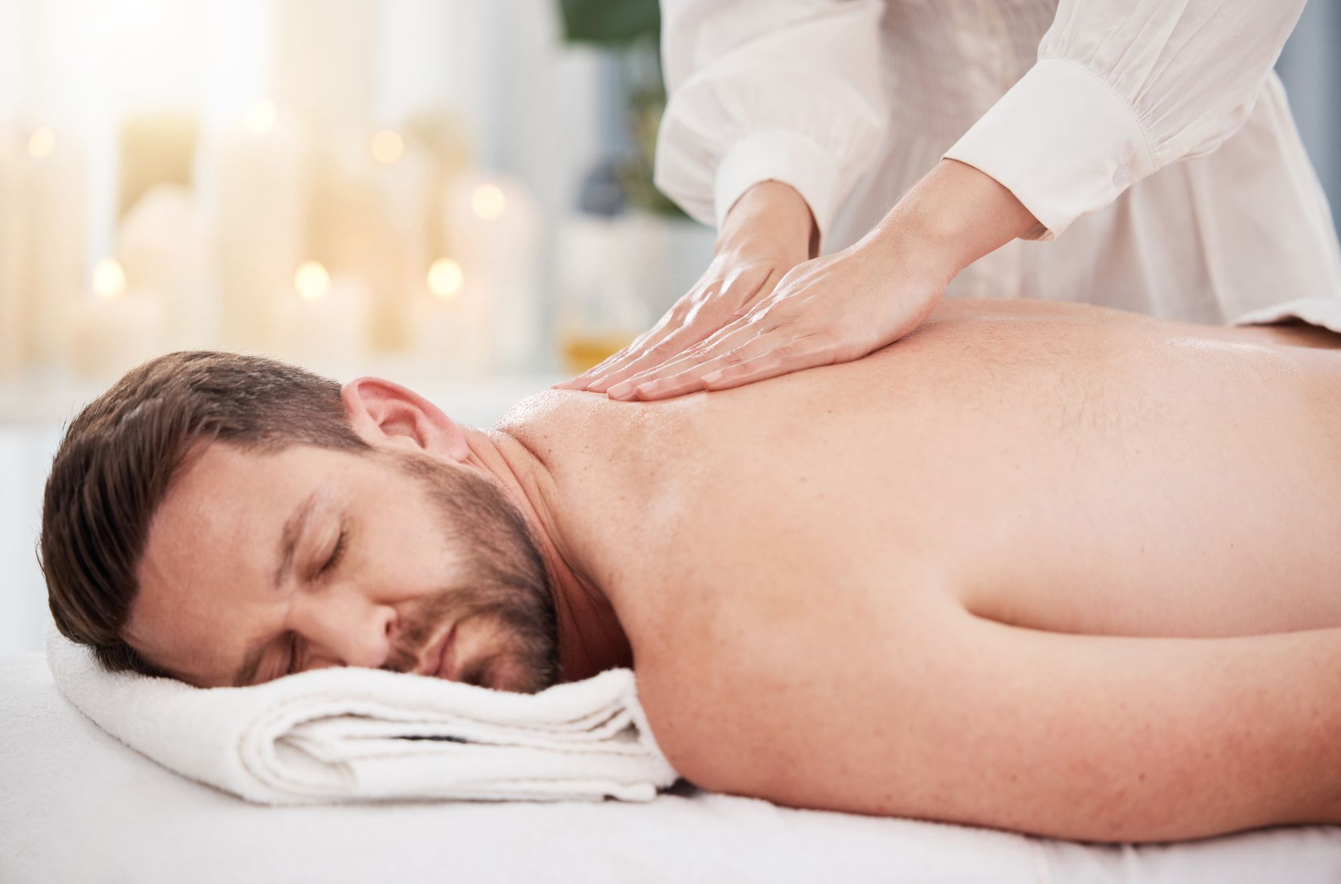 Massage therapist giving back massage to a resting client on a spa table
