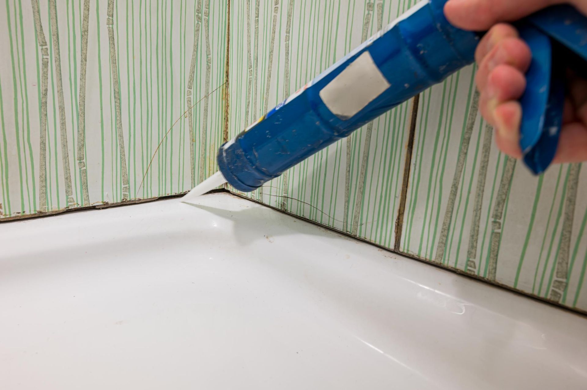 Person Applying Caulk Between a White Tub and Green-tiled Wall — AB QUICK Painting & Maintenance Services In Mareeba, QLD