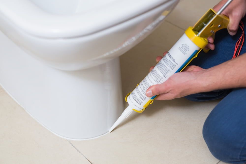 Person Applying Sealant Around the Base of a Toilet — AB QUICK Painting & Maintenance Services In Mareeba, QLD