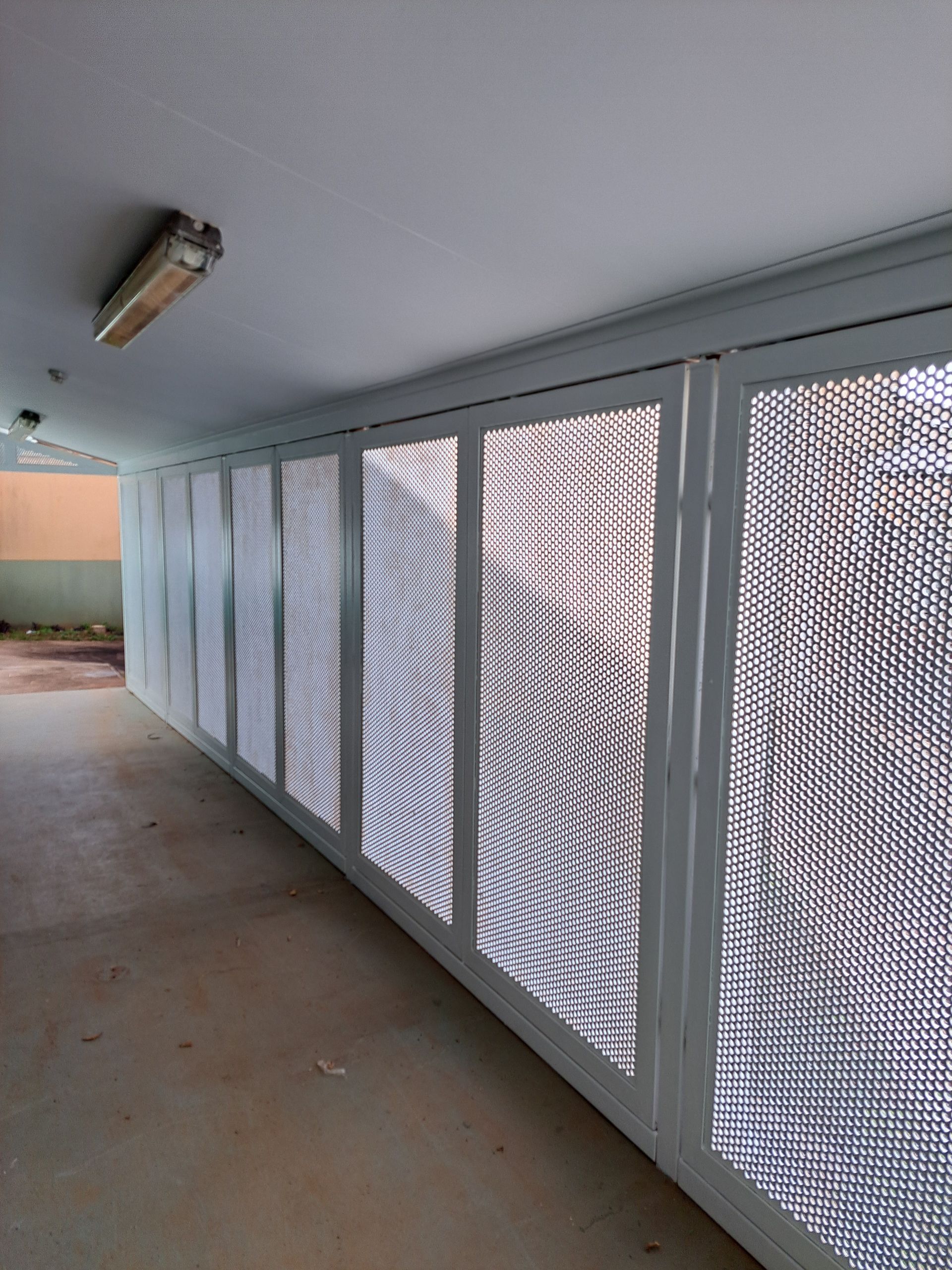 Long hallway with white screened panels on one side and a bare concrete floor.