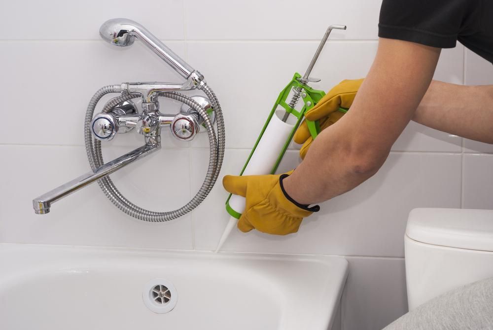 Person Caulking a Bathtub With a Caulk Gun in a Bathroom — AB QUICK Painting & Maintenance Services In Mareeba, QLD