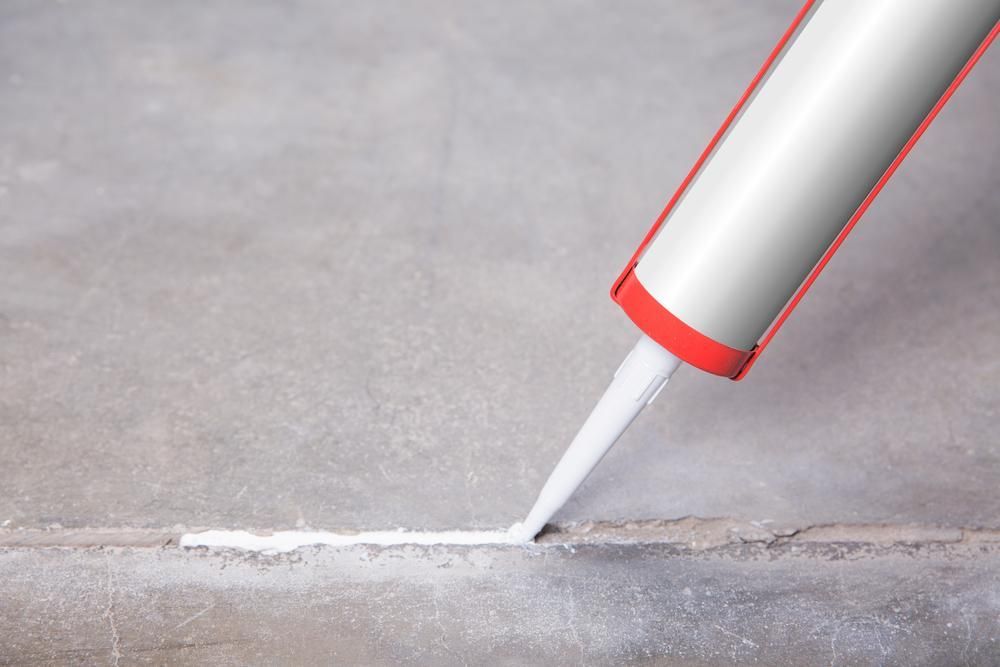 Caulk Gun Dispensing White Sealant Into a Crack in a Surface — AB QUICK Painting & Maintenance Services In Mareeba, QLD