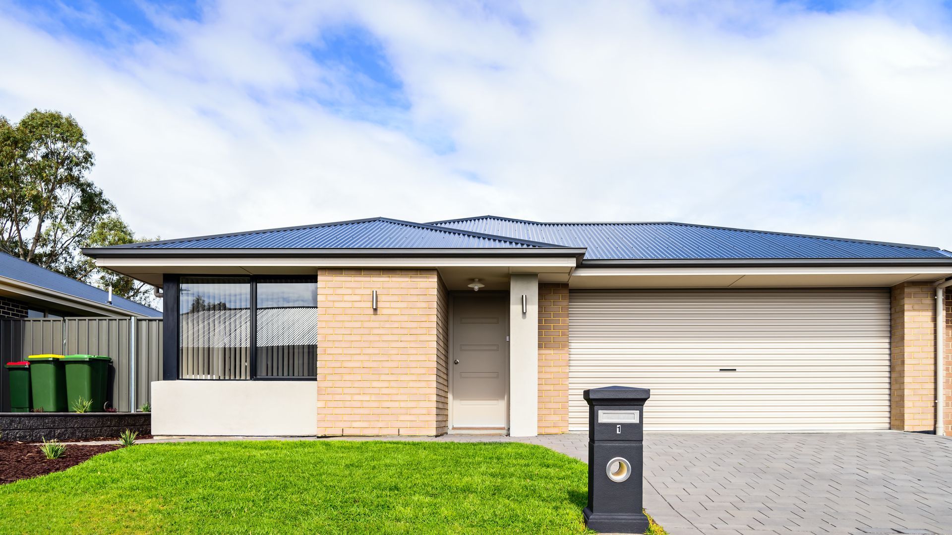 Single-story modern house with a blue roof, garage, and front lawn under a partly cloudy sky