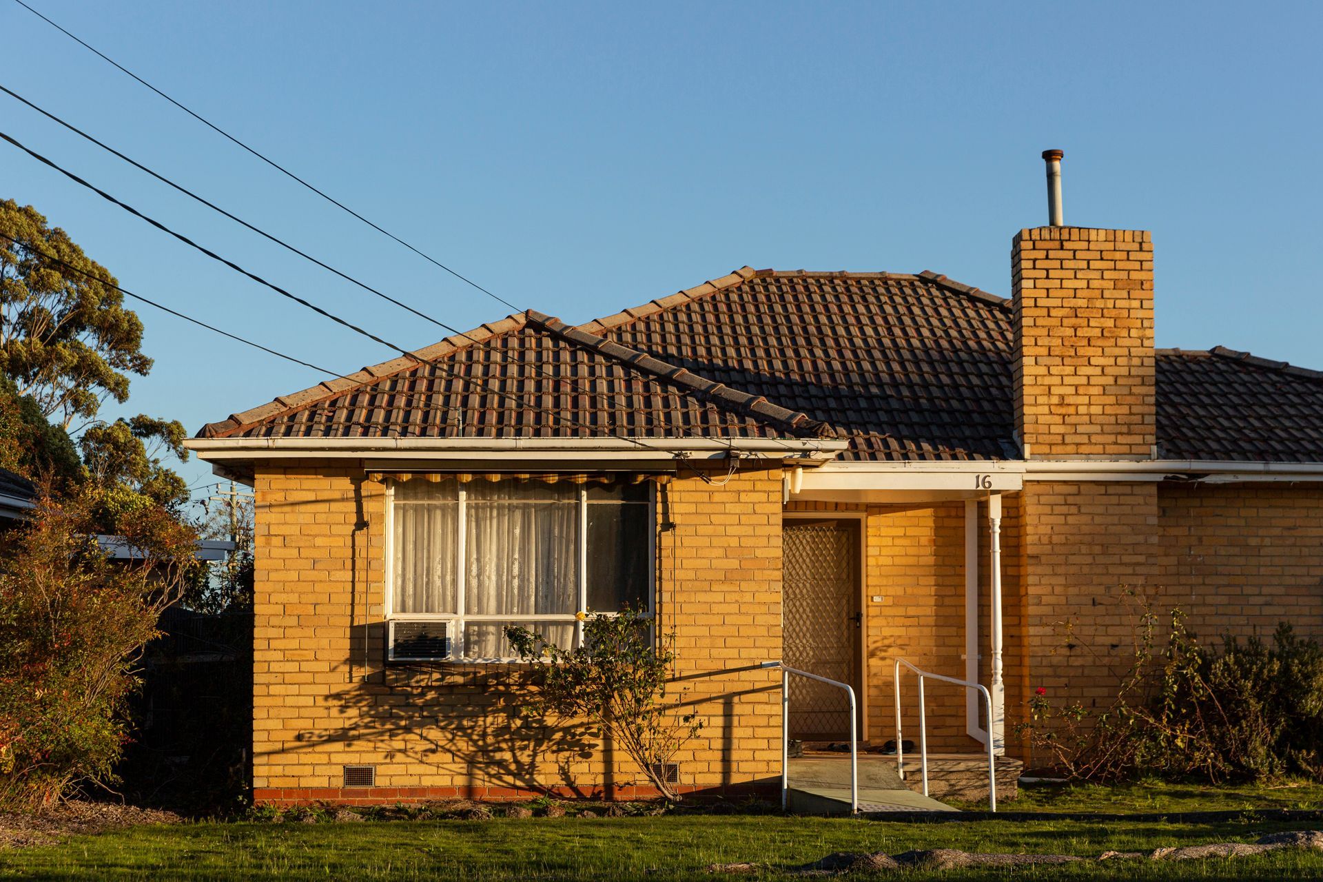 Single-story brick house with a tiled roof, front porch, and brick chimney at sunset