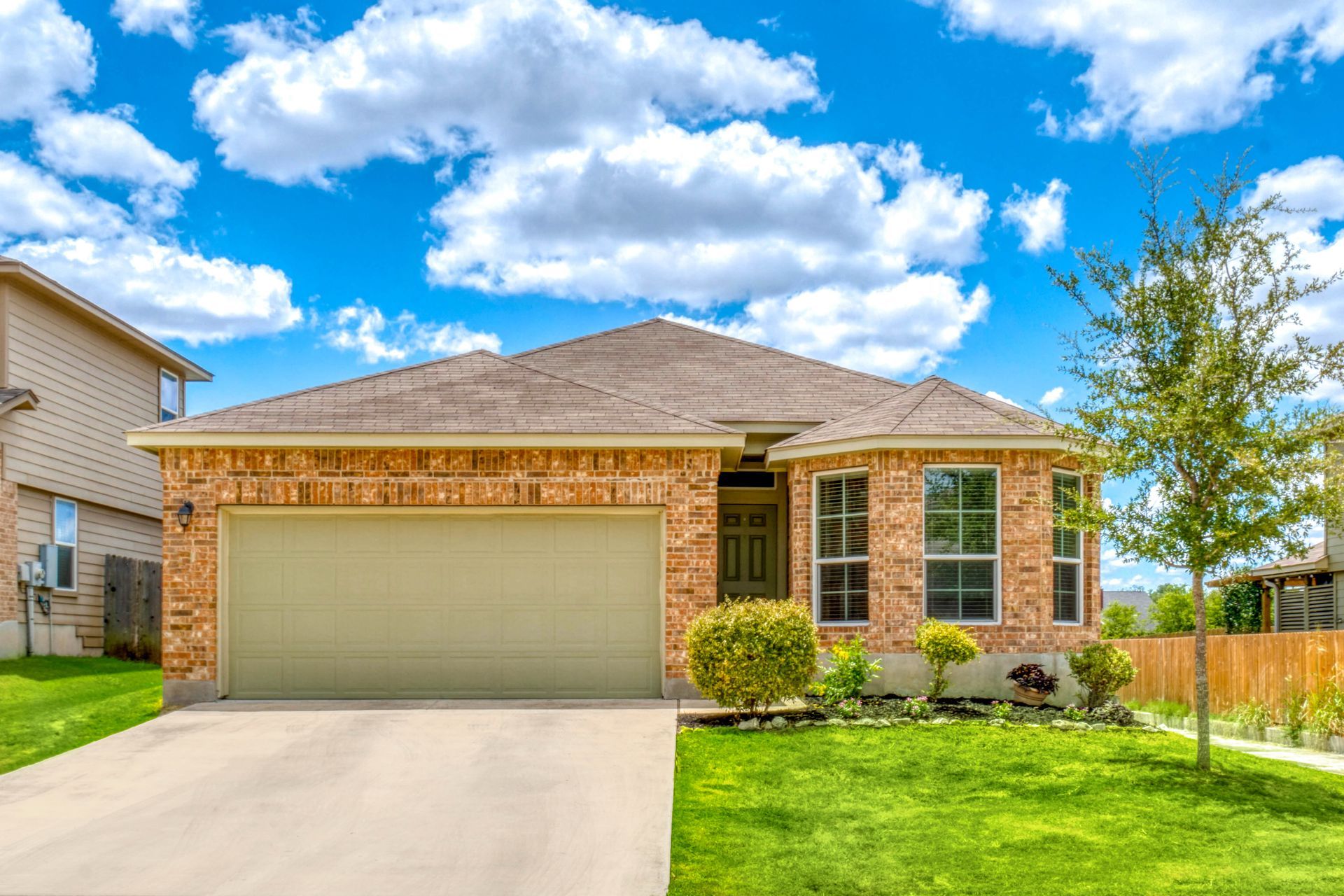 Single-story brick house with a two-car garage, front lawn, and blue sky with clouds