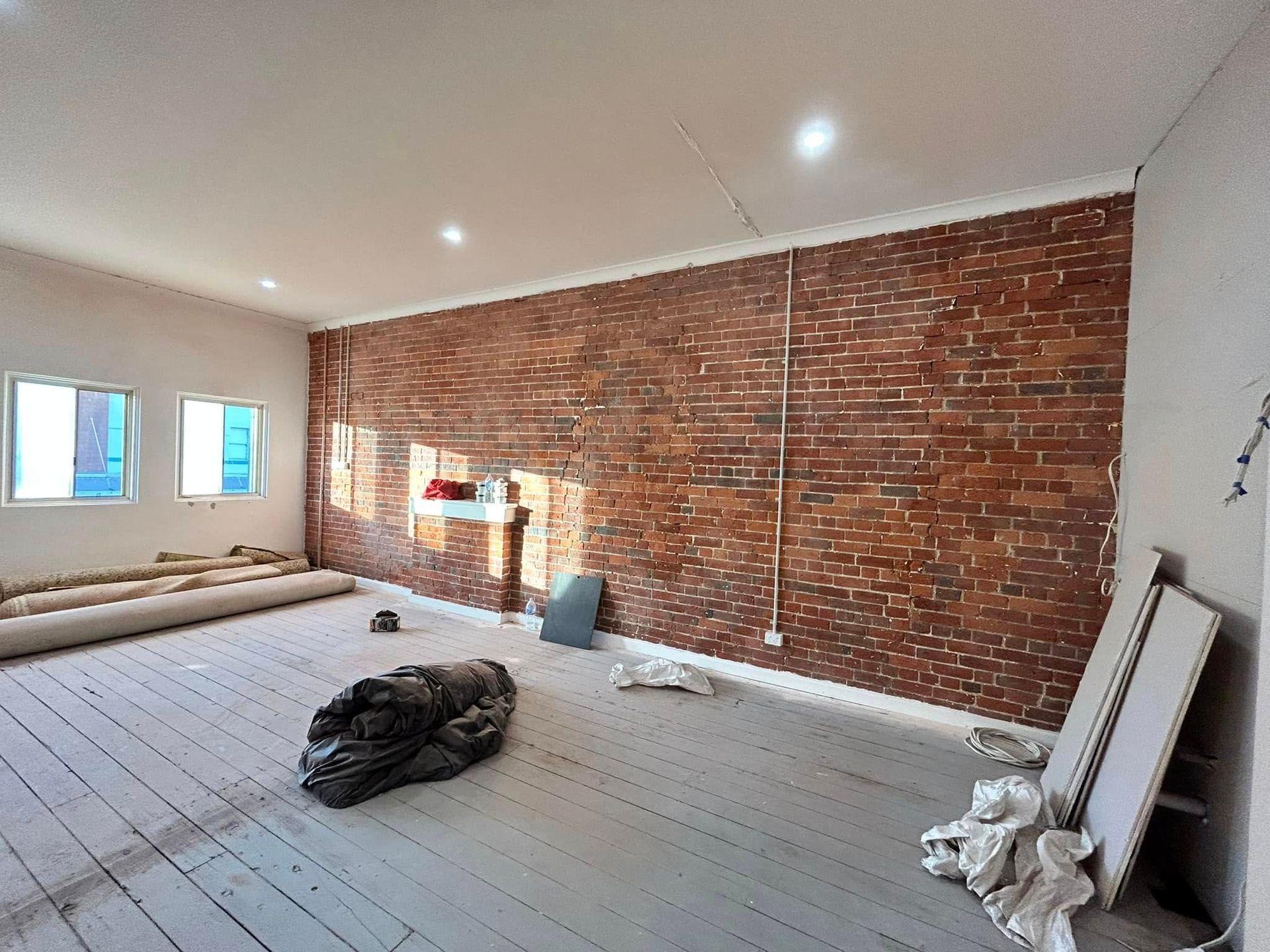 Empty room with exposed brick wall, white floor, windows, and construction materials scattered around Empty room with exposed brick wall, white floor, windows, and construction materials scattered around