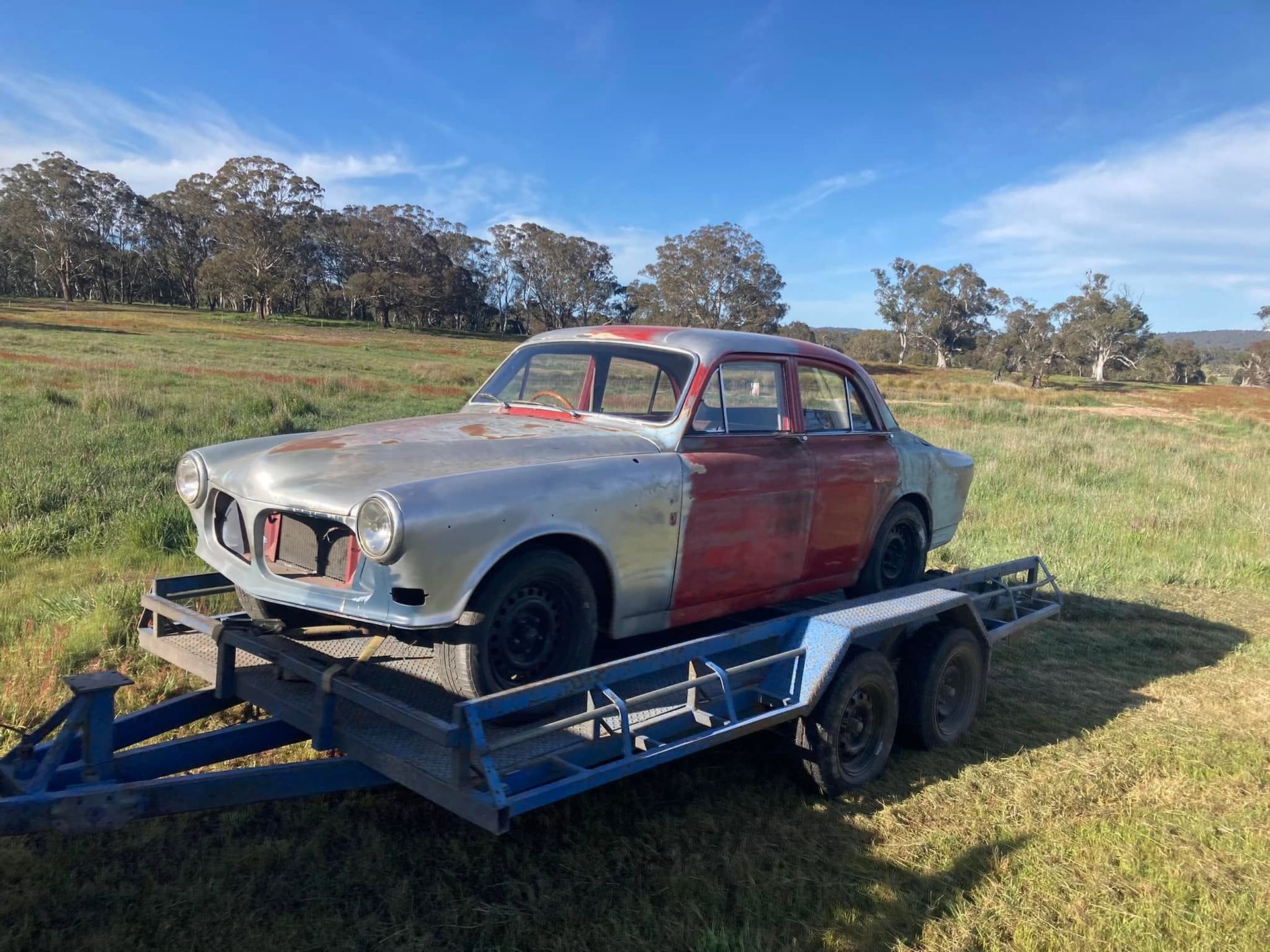 Vintage red and white car on a blue trailer in a grassy field under a clear sky.