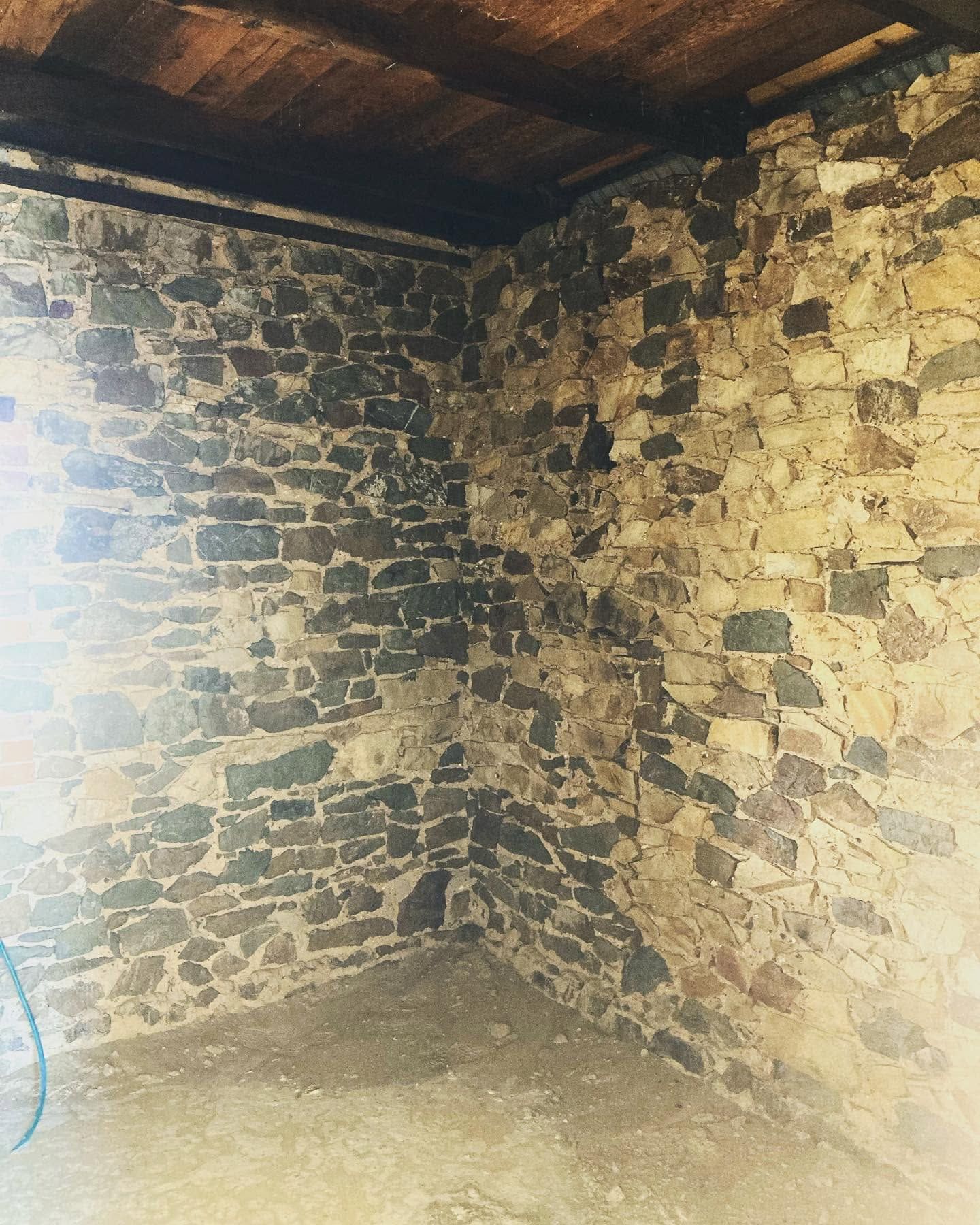 Stone-walled corner room with a wooden ceiling and a bright window on the left.