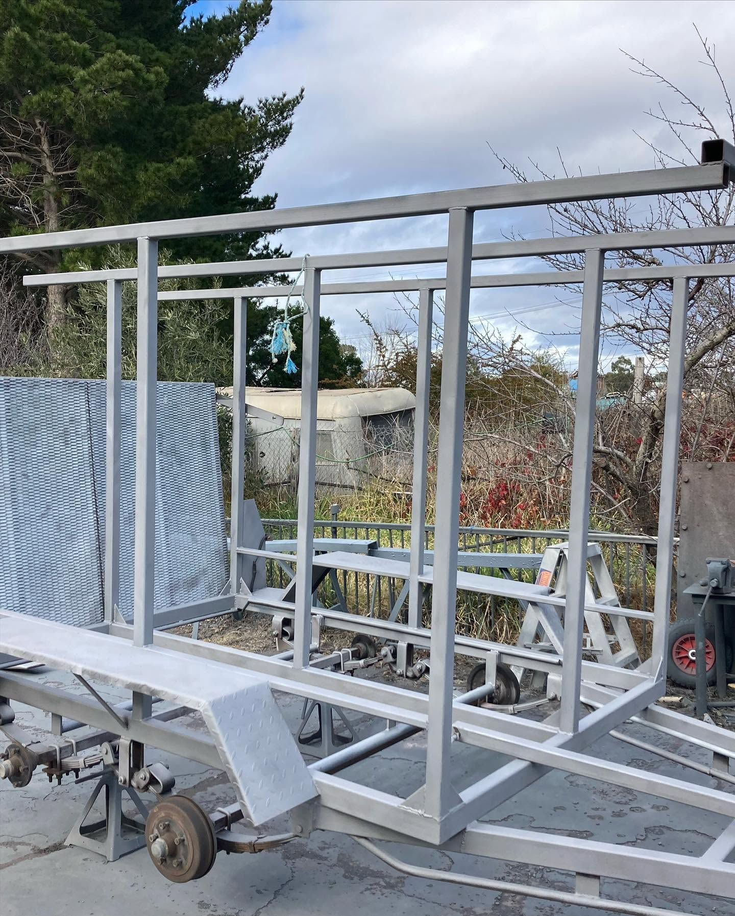 White metal trailer frame outdoors with a blue mesh side panel and wheels on the left
