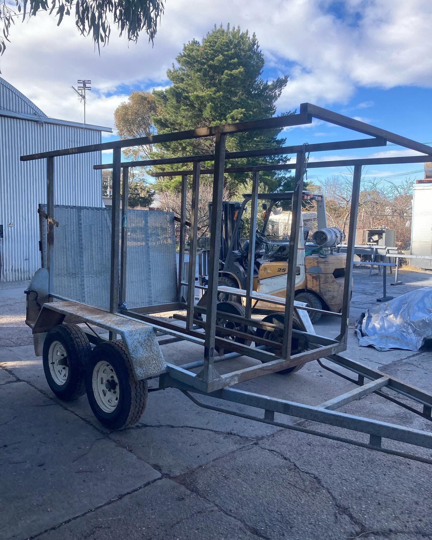 Flatbed trailer with a metal frame load parked outdoors in a yard under a blue sky.